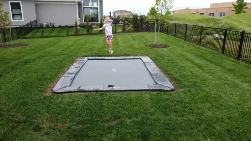 child jumping on black inground trampoline
