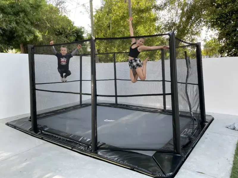 children jumping on a rectangular black trampoline with enclosure