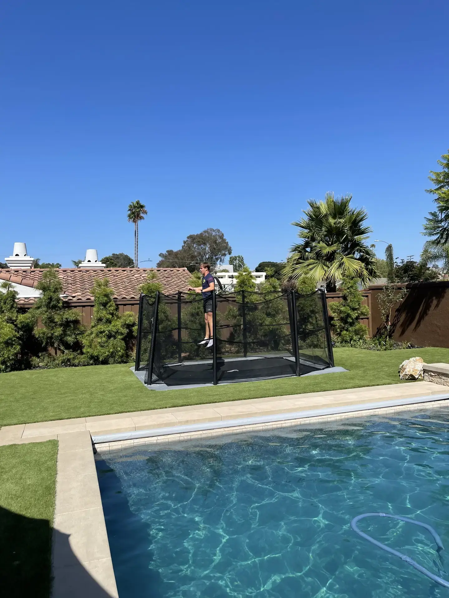 child jumping on a gray inground trampoline with enclosure