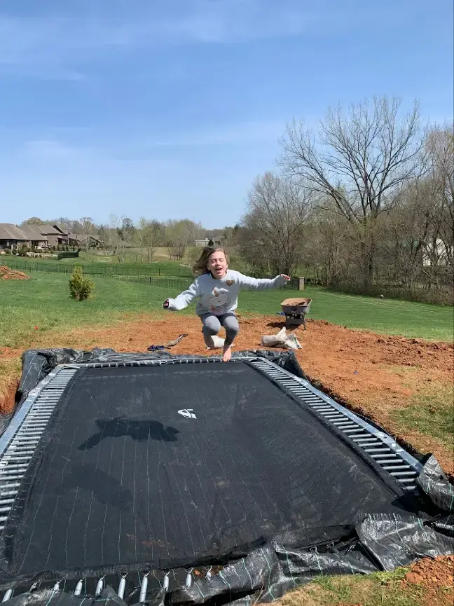A girl energetically jumps on a trampoline in a vibrant backyard, capturing the essence of childhood joy and freedom.
