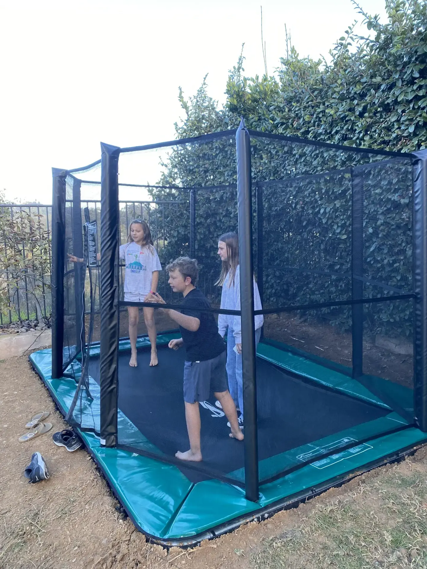 children jumping on a green inground trampoline with enclosure