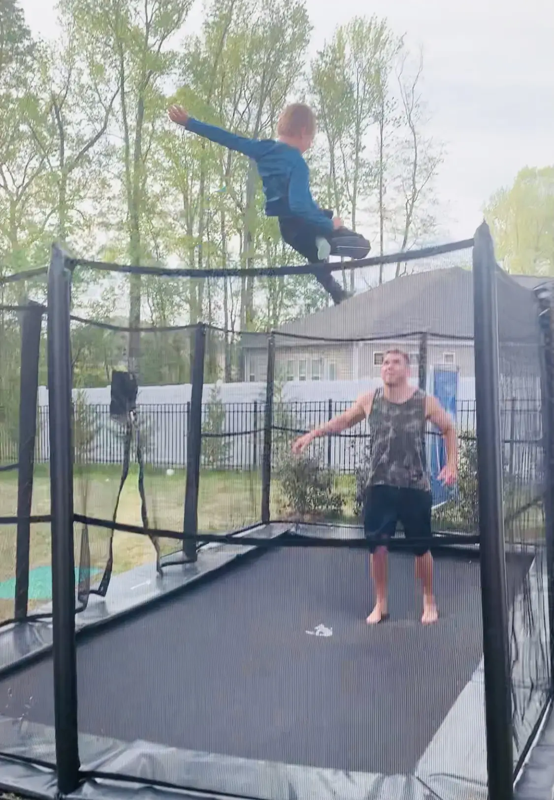 child and adult jumping on a black trampoline with enclosure